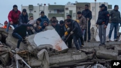 Un grupo de personas busca entre los escombros de un edificio a sobrevivientes tras un sismo, en Adana, Turquía, el lunes 6 de febrero de 2023. (AP Foto/Khalil Hamra)